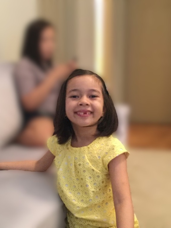 Alba in a bright yellow top with Cher seen in a blurred background. Photo was taken in a living room