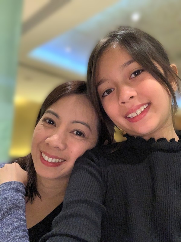 Cher and Alba leaning close and smiling gently; indoor setting with warm ambient lighting and softly lit ceiling in the background; affectionate, relaxed mood