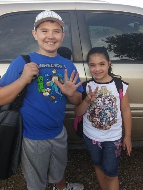 TJ and Adlynn standing in front of a car with their back packs